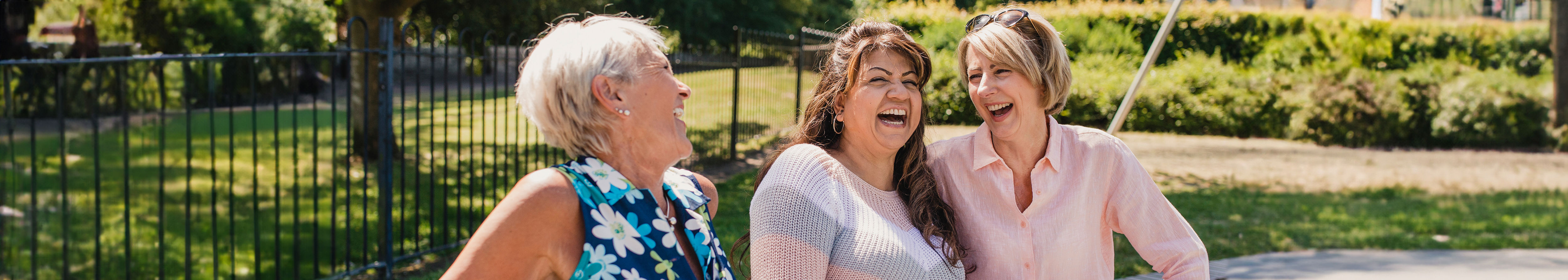 Three elderly women sitting in a park are laughing